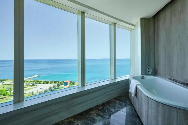 Une baignoire moderne offre une vue dégagée sur la mer depuis une grande fenêtre.