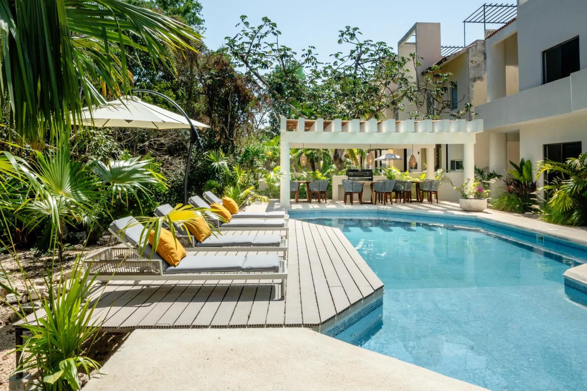 Transats et parasols bordent une piscine rectangulaire dans un jardin tropical.