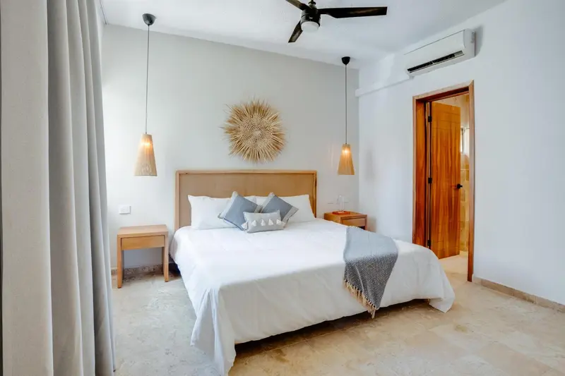 Une chambre lumineuse avec un grand lit recouvert de linge blanc et décorée d'un motif mural en fibres naturelles.