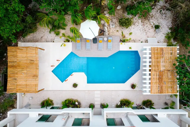 Vue aérienne d'une piscine rectangulaire entourée de chaises longues et de végétation.