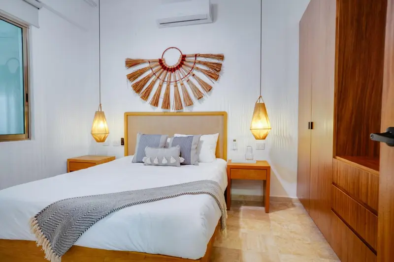Une chambre lumineuse avec un grand lit recouvert d'une couverture texturée et décorée de coussins.