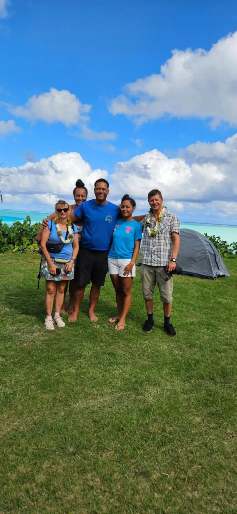 Groupe de personnes souriantes posant sur une pelouse verdoyante face à la mer.