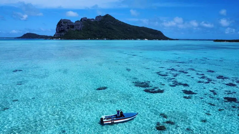 Un bateau navigue sur une eau turquoise peu profonde près d'une île verdoyante.