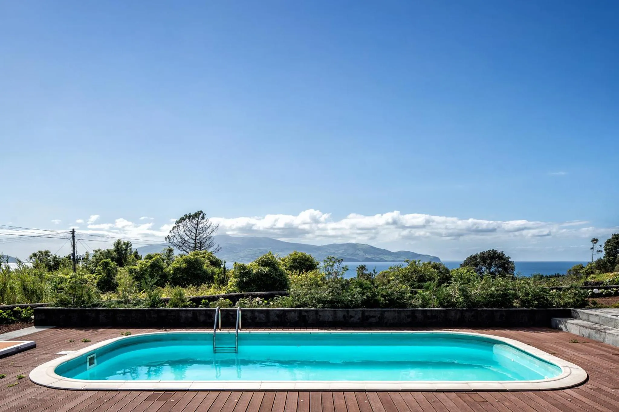 Une piscine rectangulaire avec terrasse en bois offre une vue sur la mer et les montagnes.