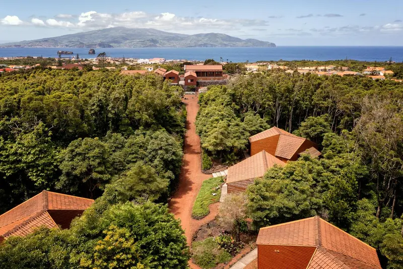 Vue aérienne d'un ensemble de bâtiments aux toits rouges entourés d'une végétation luxuriante, avec une île en arrière-plan.