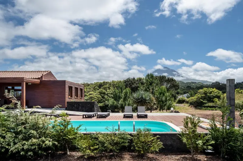 Une piscine turquoise bordée d'une terrasse en bois, avec un bâtiment moderne en arrière-plan et une végétation luxuriante.