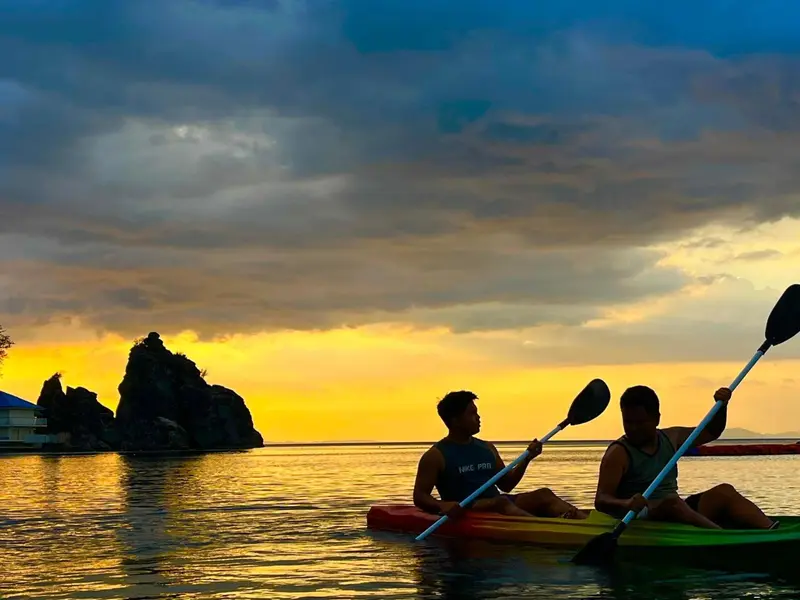 Deux personnes pagayent en kayak sur une mer calme au coucher du soleil.