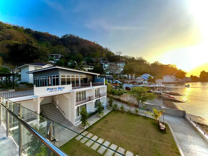 Vue aérienne d'un bâtiment blanc avec une terrasse surplombant une baie au coucher du soleil.