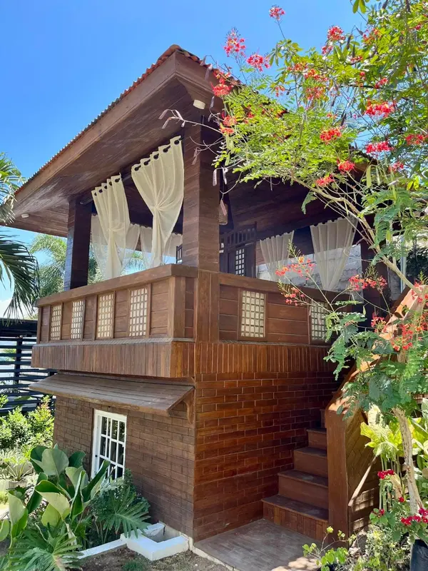 Petite maison en bois sur pilotis avec balcon fleuri et escalier d'accès.