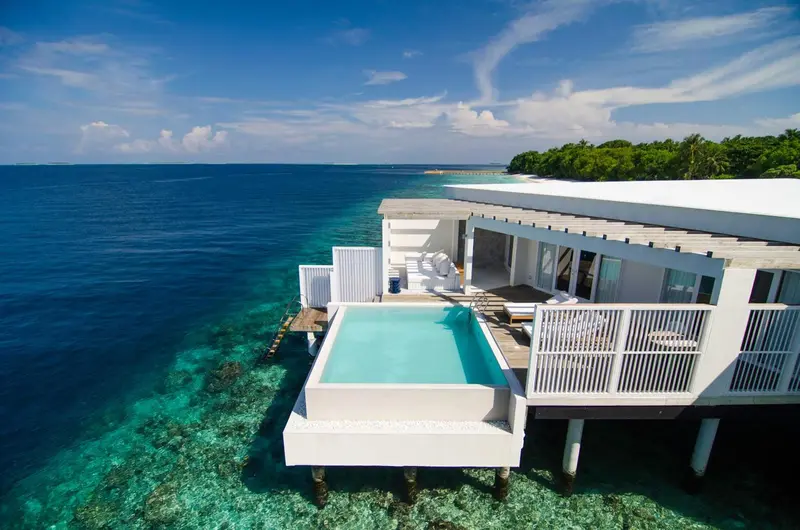 Vue aérienne d'une terrasse avec piscine privée sur pilotis au-dessus d'un lagon turquoise.