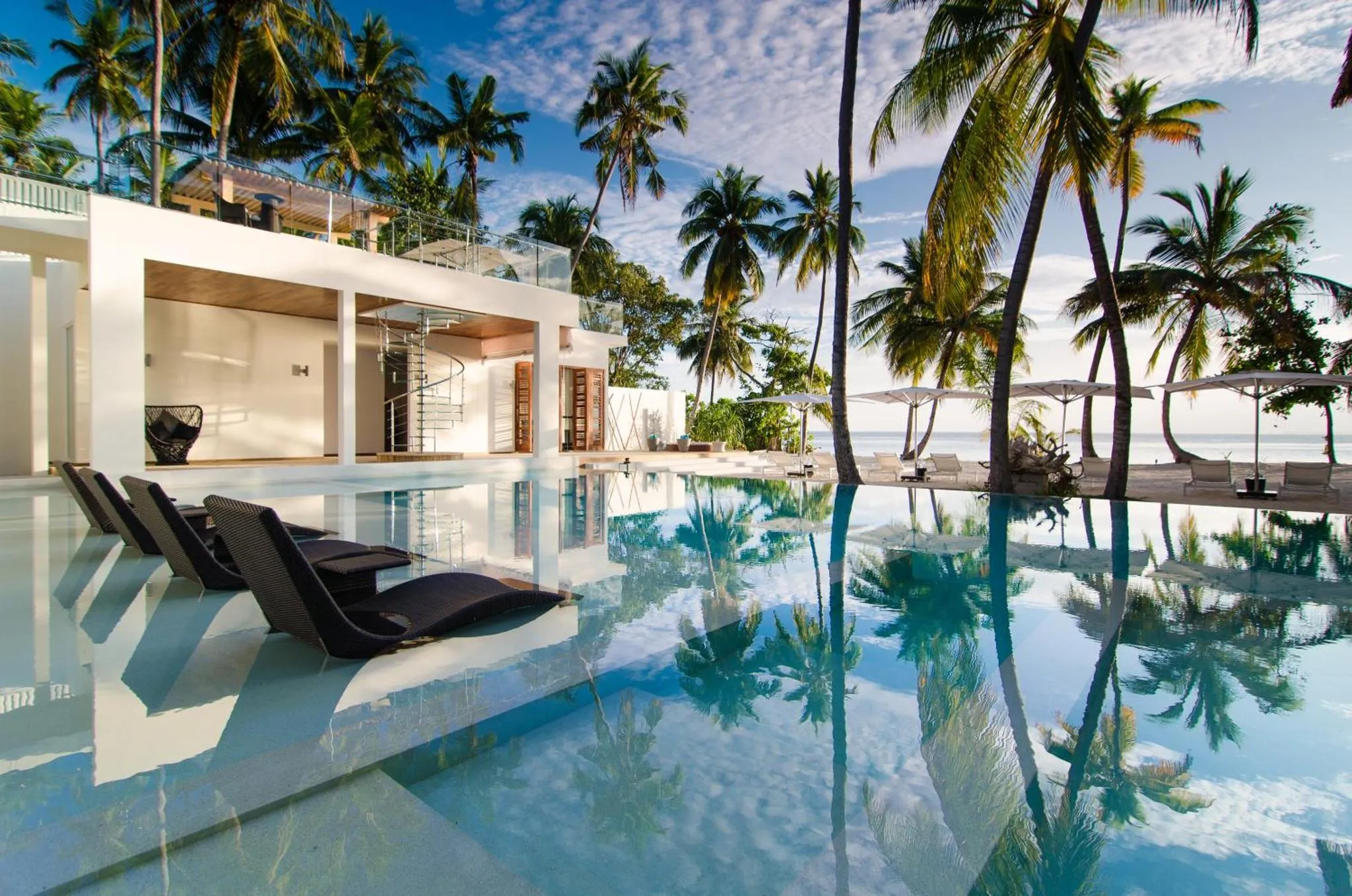 Transats noirs au bord d'une piscine turquoise avec vue sur la mer et les palmiers.