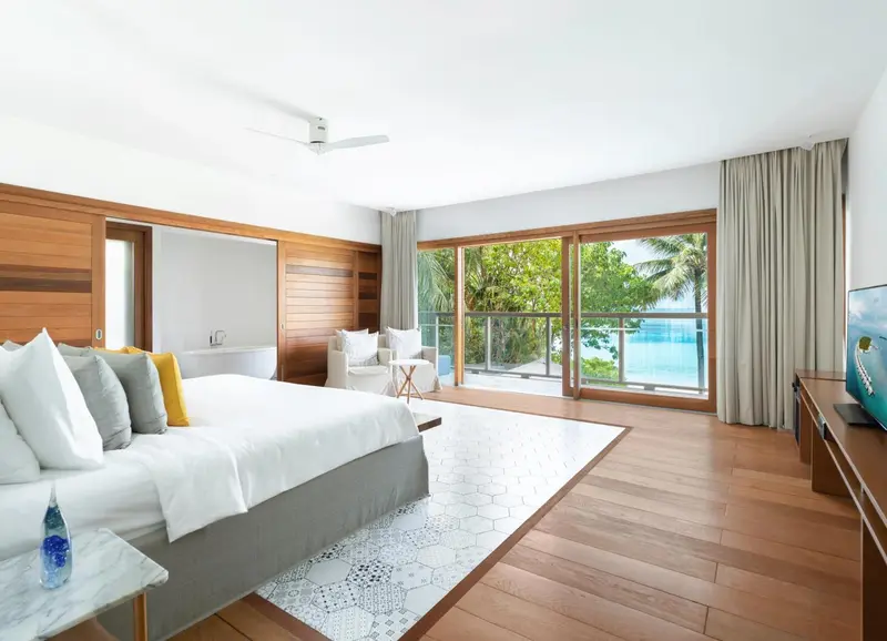 Une chambre lumineuse avec un grand lit donnant sur une terrasse et la mer.