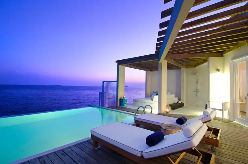 Terrasse avec piscine et mobilier de détente face à la mer au crépuscule.