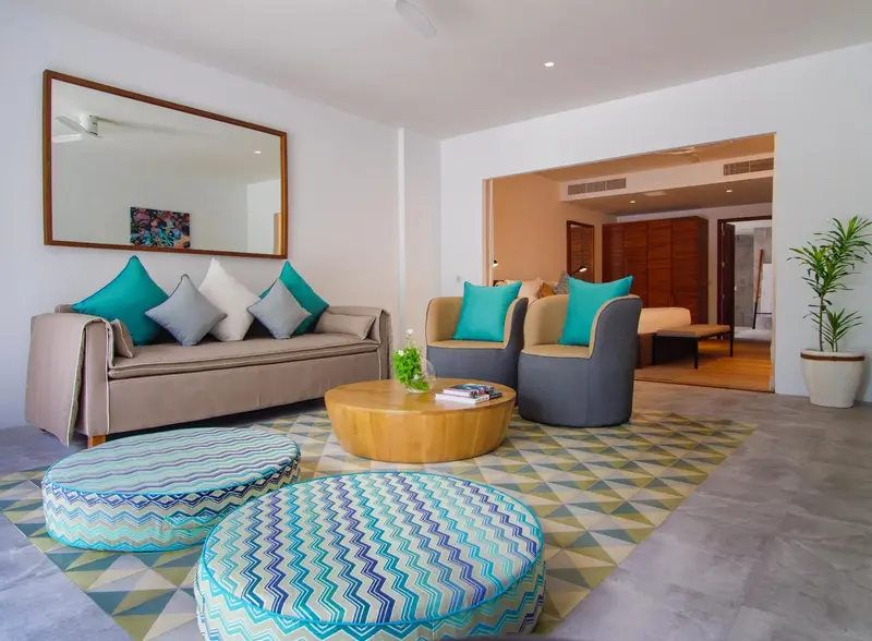 Un salon clair avec canapés et poufs colorés.