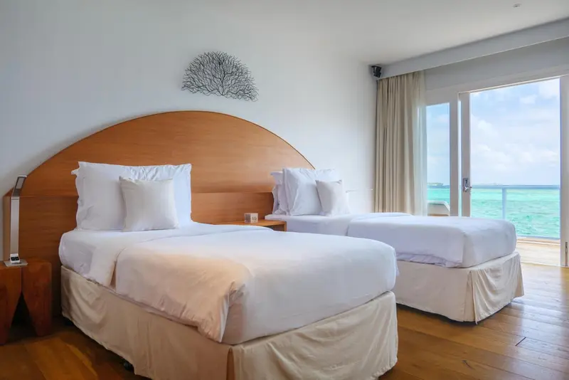 Chambre lumineuse avec deux lits simples et vue sur la mer.