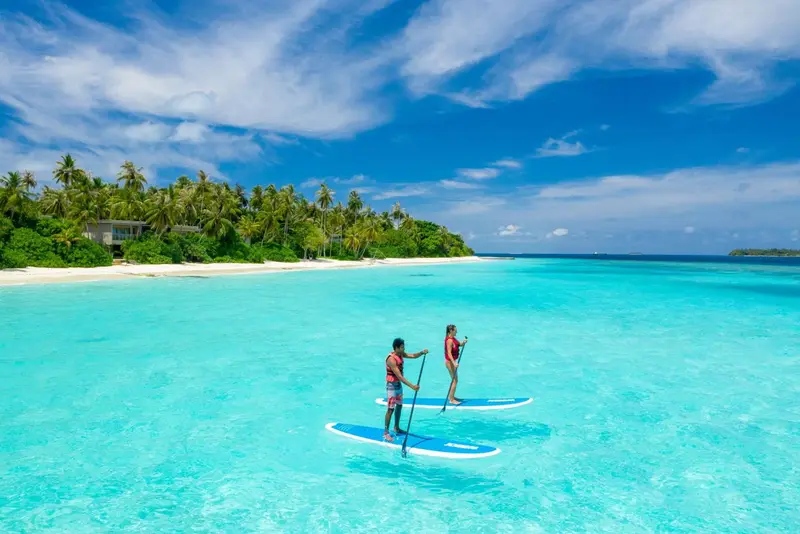 Deux personnes pratiquent le paddleboard dans une eau turquoise peu profonde.
