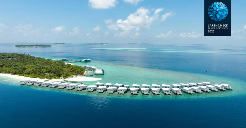 Vue aérienne d'un complexe hôtelier de luxe avec des villas sur pilotis au-dessus d'un lagon turquoise.