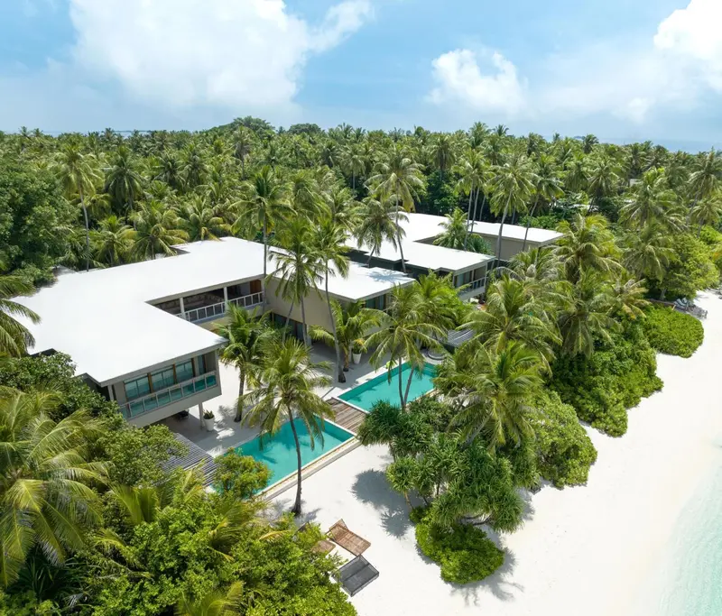 Vue aérienne d'un complexe hôtelier blanc entouré de végétation luxuriante et bordé d'une plage de sable fin.