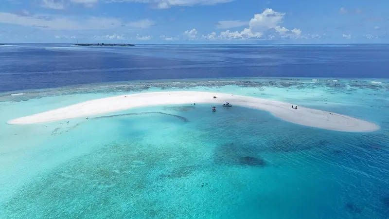 Vue aérienne d'un îlot de sable blanc entouré d'eaux turquoise et d'un récif corallien.