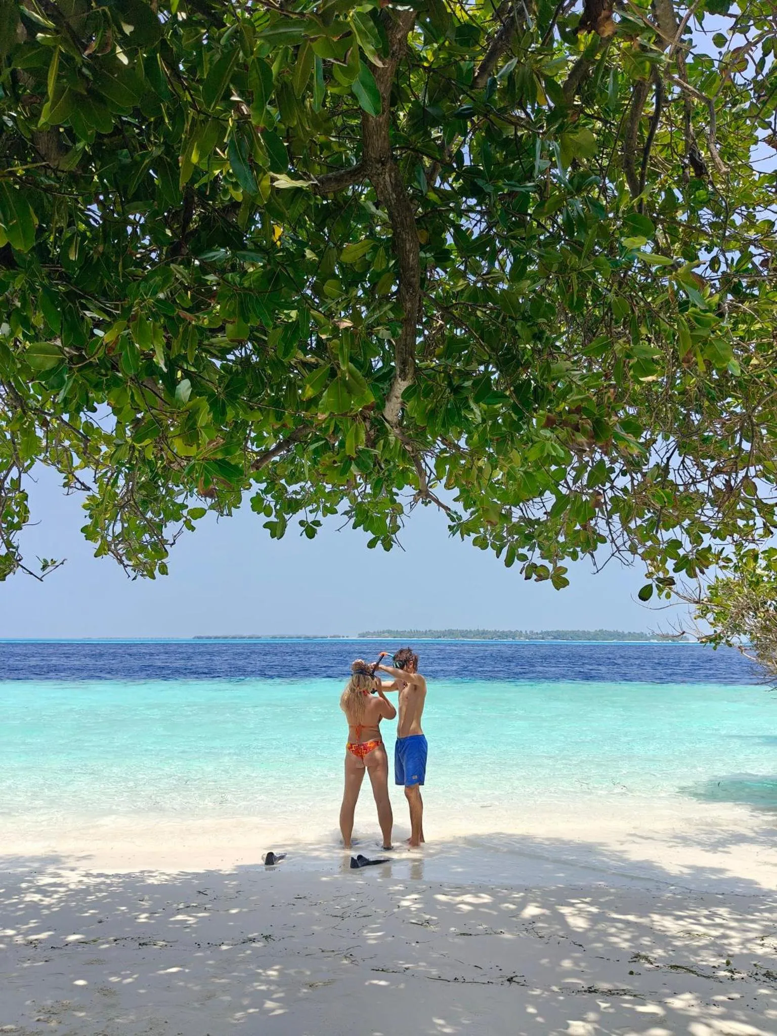Deux personnes se tiennent sur une plage de sable blanc face à la mer turquoise.