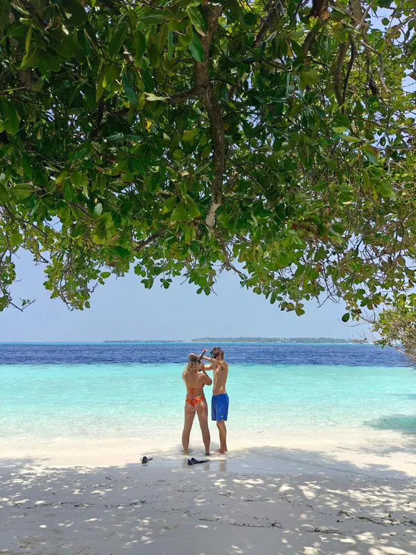 Deux personnes se tiennent sur une plage de sable blanc face à la mer turquoise.