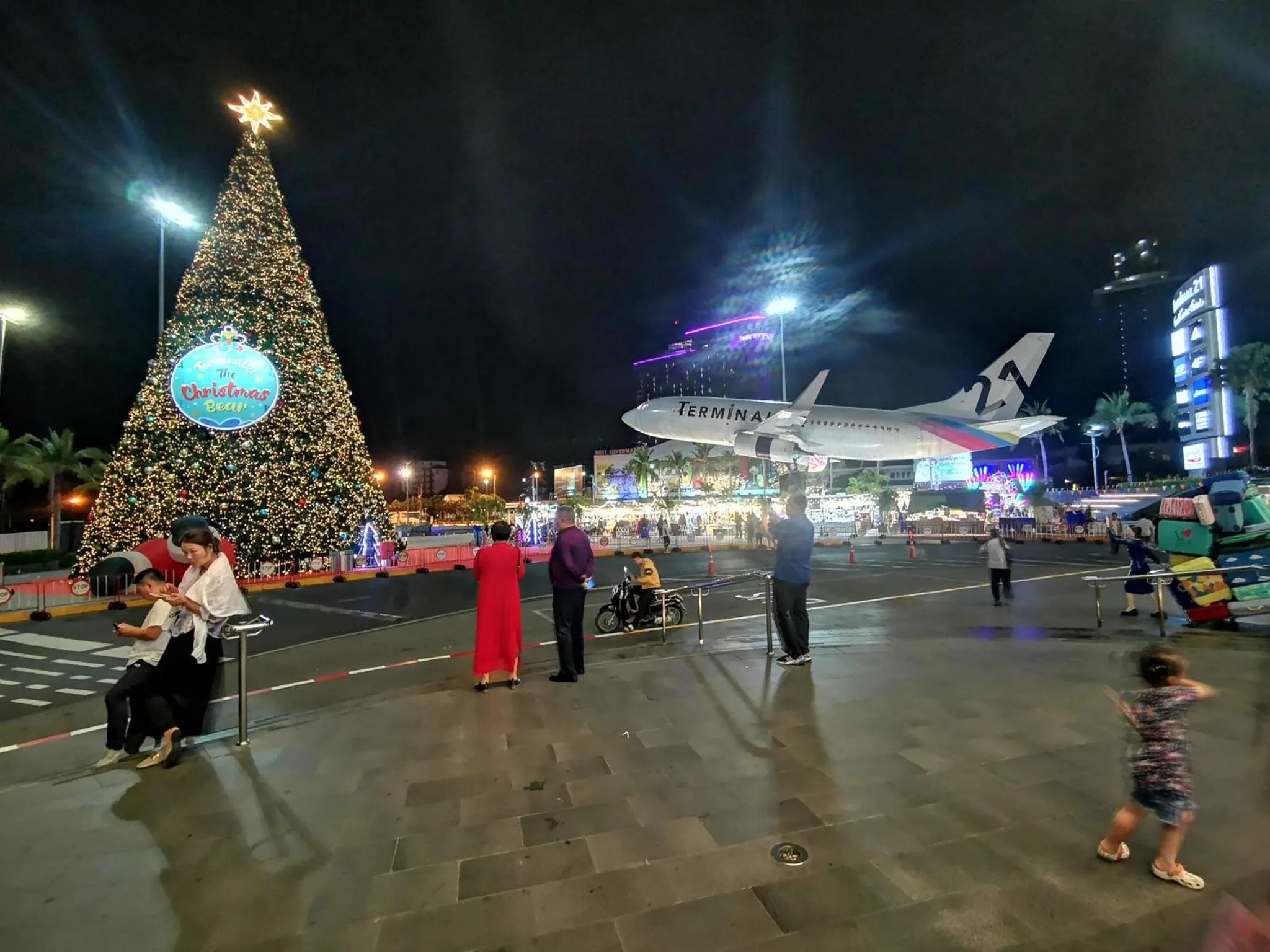 Une vue nocturne d'un aéroport illuminé avec un sapin de Noël et un avion.