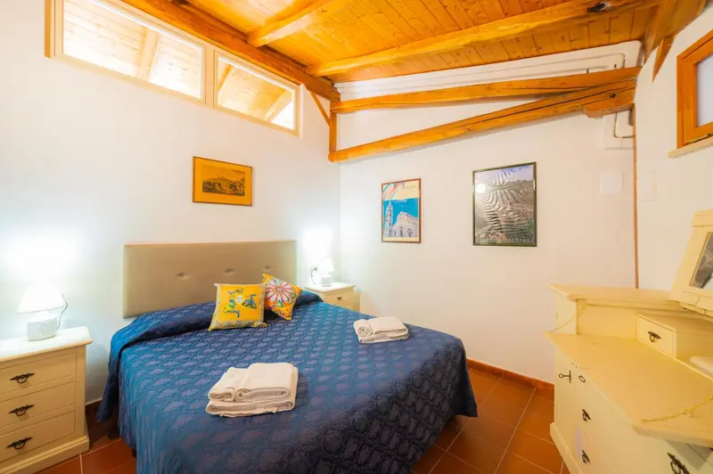 Une chambre lumineuse avec un grand lit recouvert d'une couverture bleue et de coussins colorés.