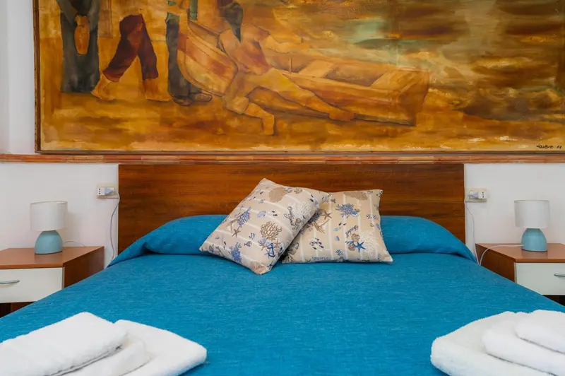 Une chambre lumineuse avec un grand lit recouvert d'une courtepointe bleue et de coussins décoratifs.