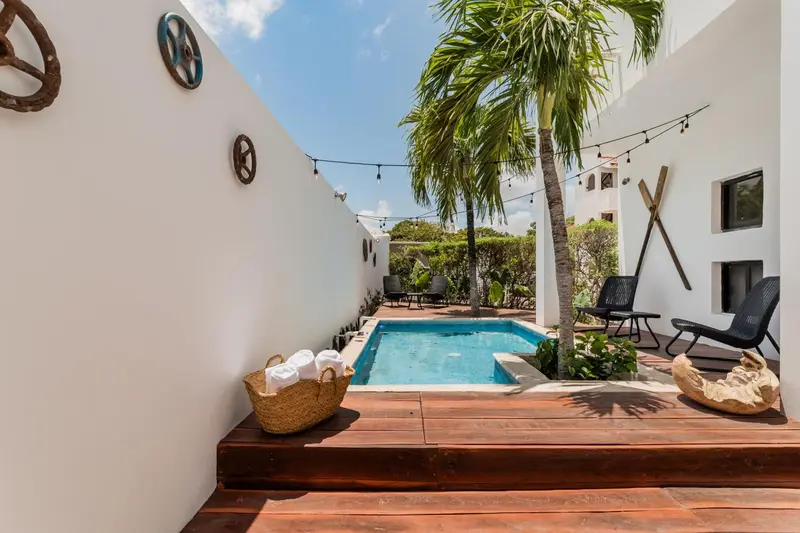 Petite piscine rectangulaire entourée d'une terrasse en bois et de végétation tropicale.
