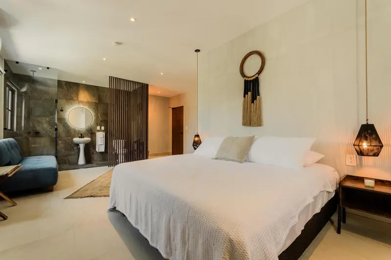 Une chambre lumineuse avec un grand lit et un espace douche ouvert.
