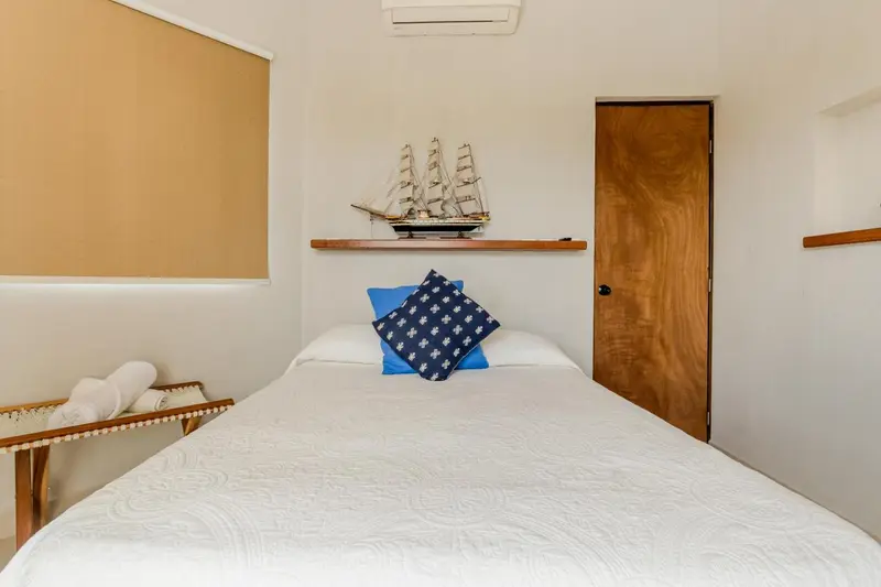Une chambre lumineuse avec un lit fait et un modèle de bateau sur une étagère.