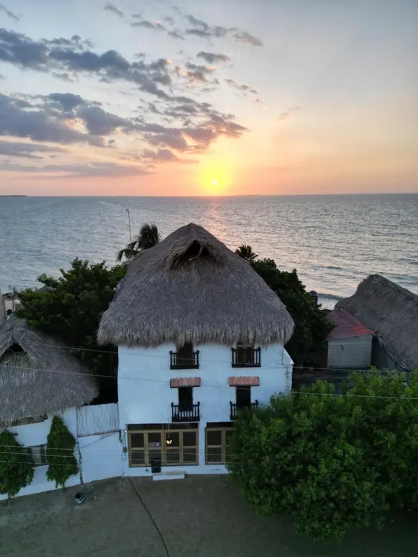 Bâtiment blanc avec toit de chaume face à la mer au coucher du soleil.
