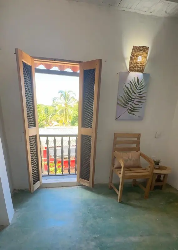 Une chaise en bois est placée devant une fenêtre ouverte donnant sur une végétation luxuriante.