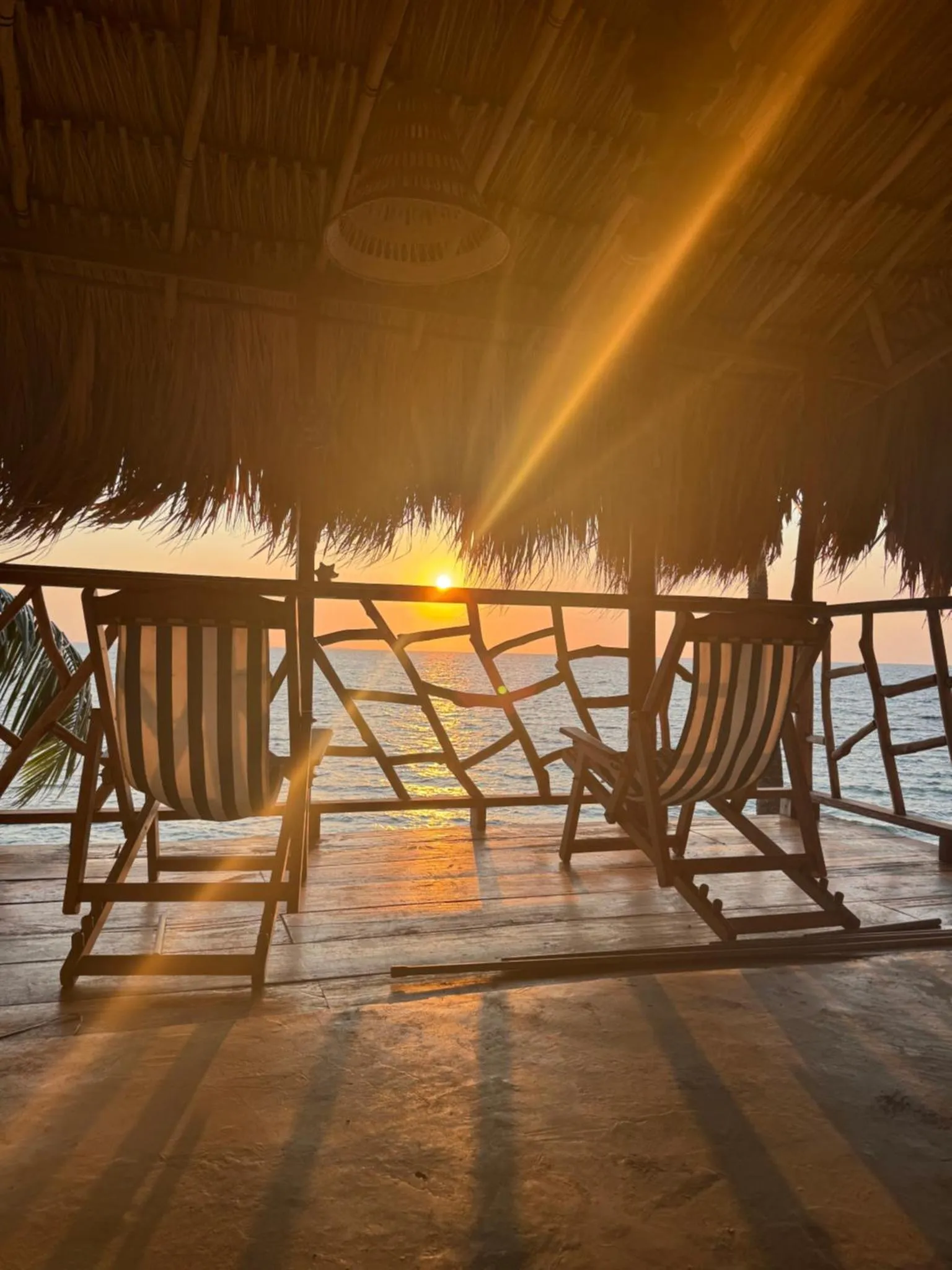 Deux transats en bois se trouvent sur une terrasse en bois face à la mer au coucher du soleil.