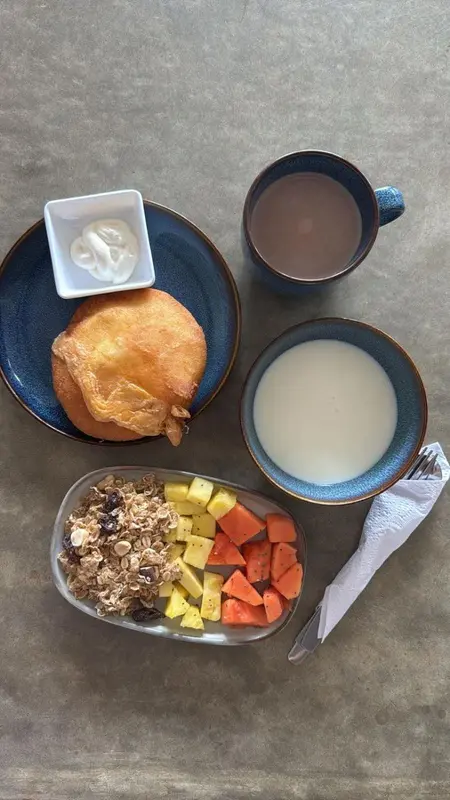 Un petit-déjeuner composé de yaourt, de céréales, de fruits frais et de viennoiseries est présenté sur une table.