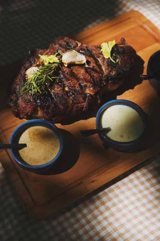 Une viande grillée est présentée sur une planche en bois avec des sauces en accompagnement.