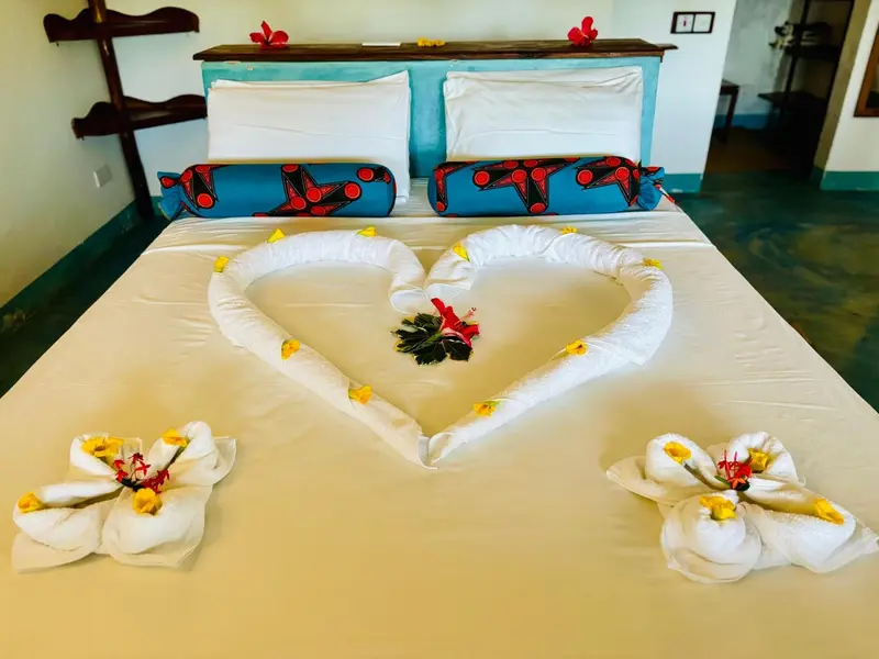 Lit double décoré de fleurs et de serviettes en forme de cœur dans une chambre.