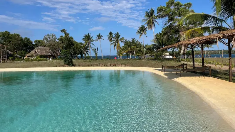 Une piscine turquoise bordée d'une plage de sable fin sous des palmiers.