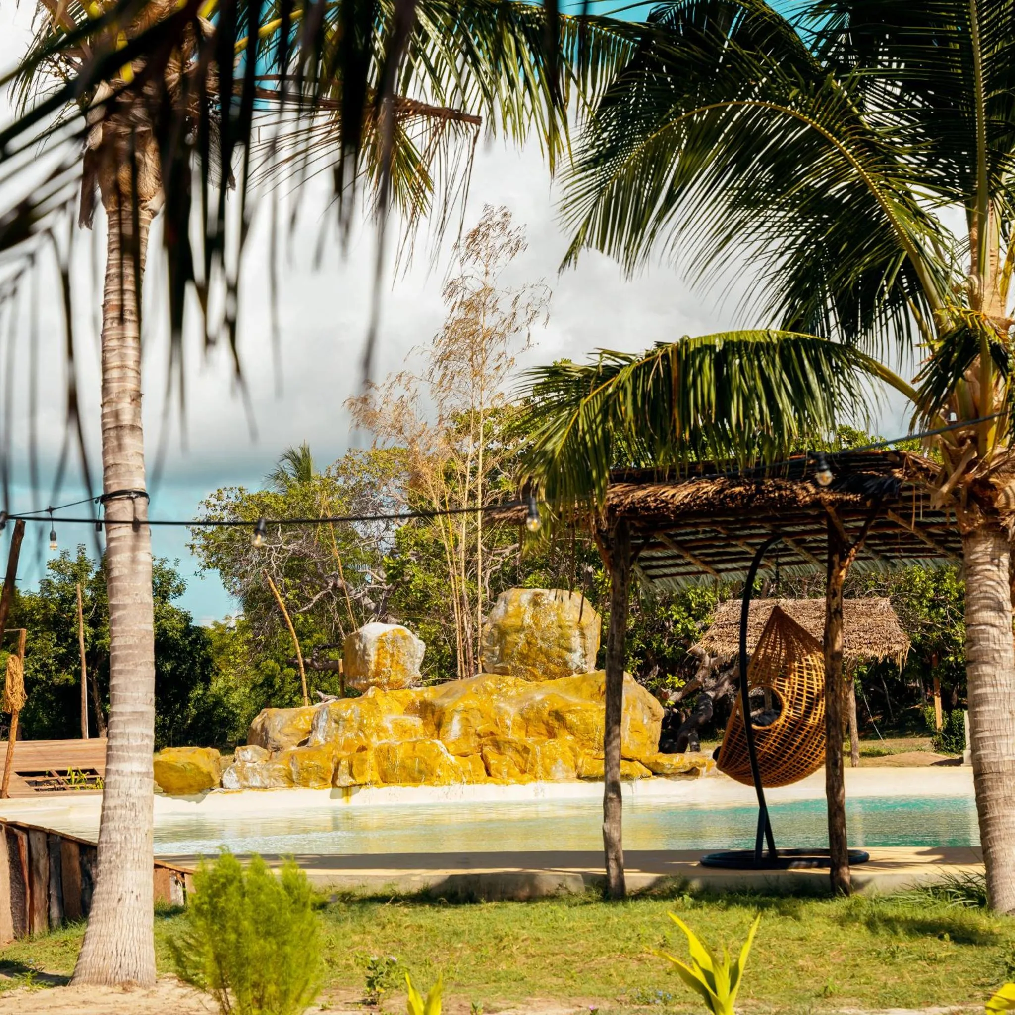 Une piscine bordée de végétation tropicale et d'un espace de détente ombragé.