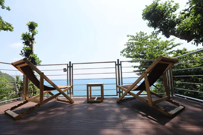 Deux chaises longues en bois sur une terrasse ensoleillée avec vue sur la mer.