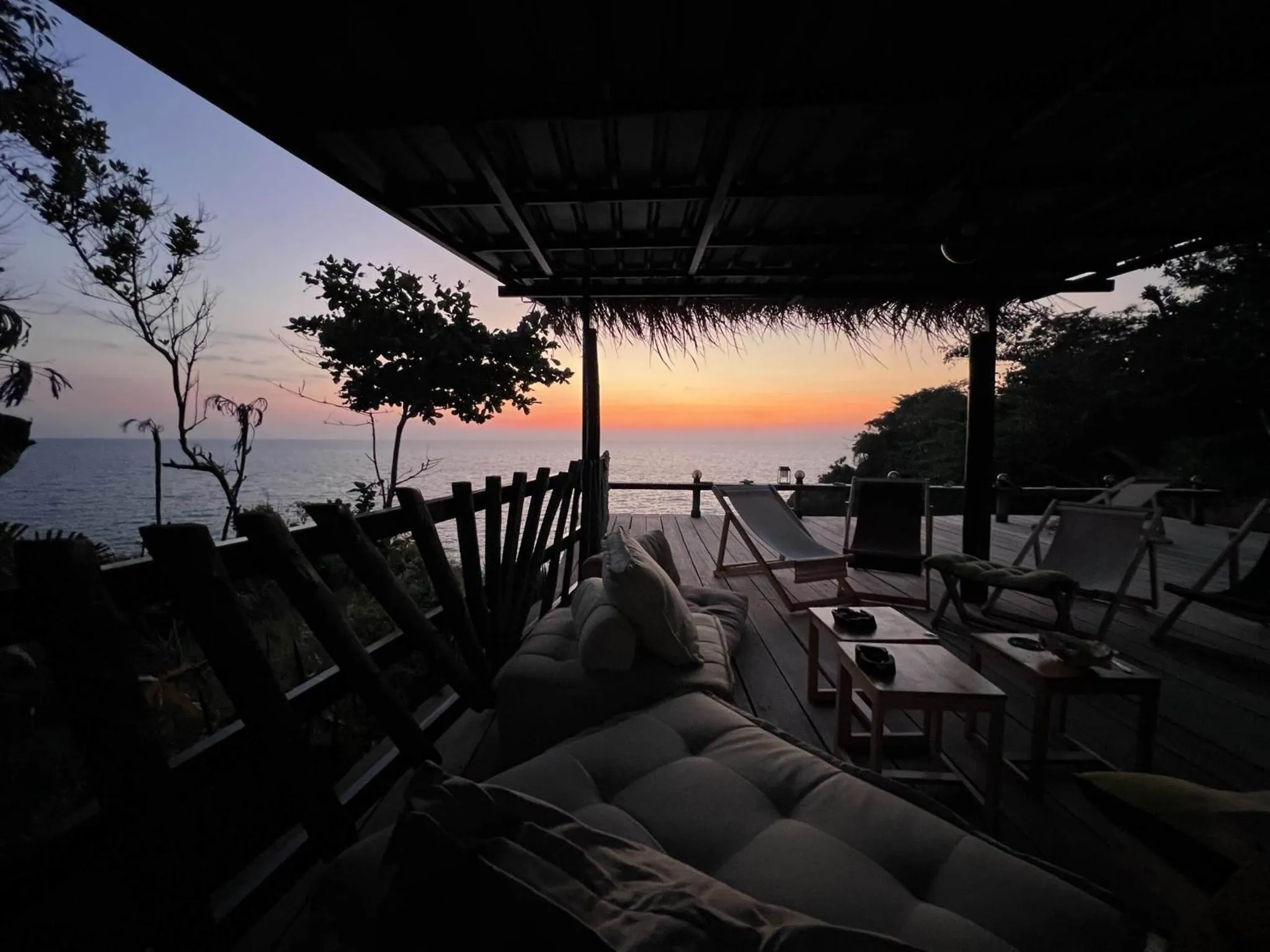 Terrasse ombragée avec mobilier de détente face à la mer au coucher du soleil.