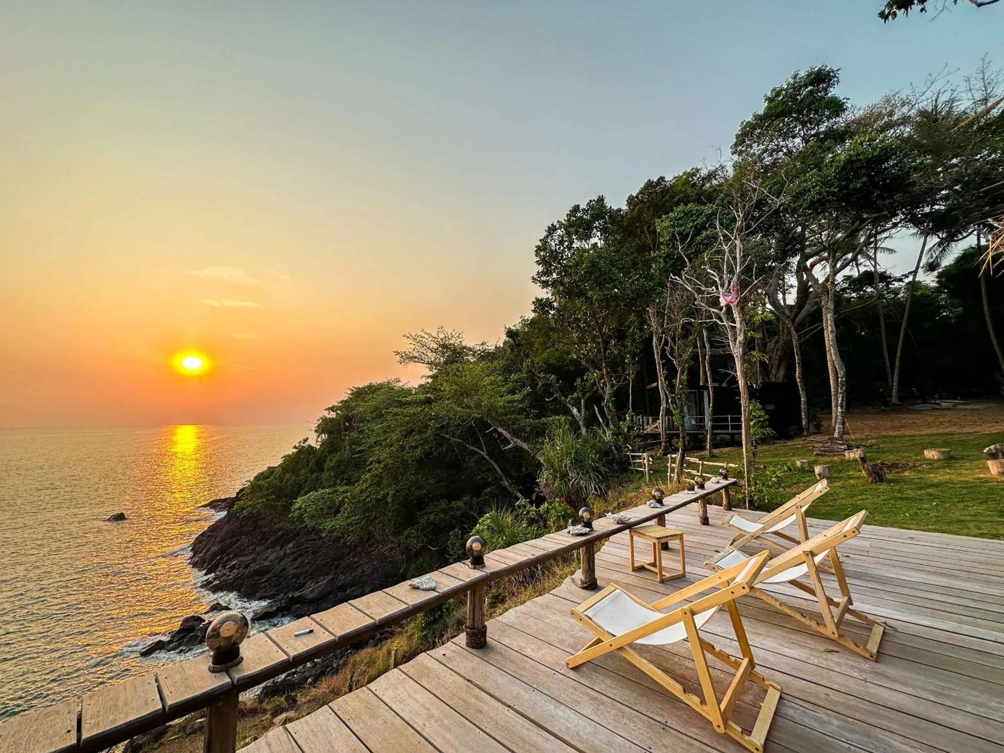 Terrasse en bois avec transats face à la mer au coucher du soleil.
