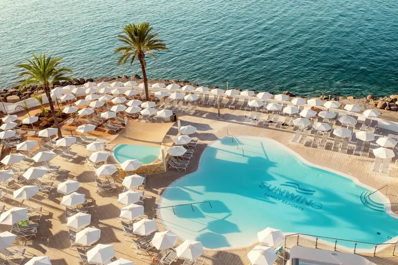 Vue aérienne d'une plage avec des transats et une piscine turquoise.