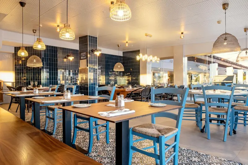 Une salle de restaurant lumineuse avec des tables bleues et des suspensions décoratives.