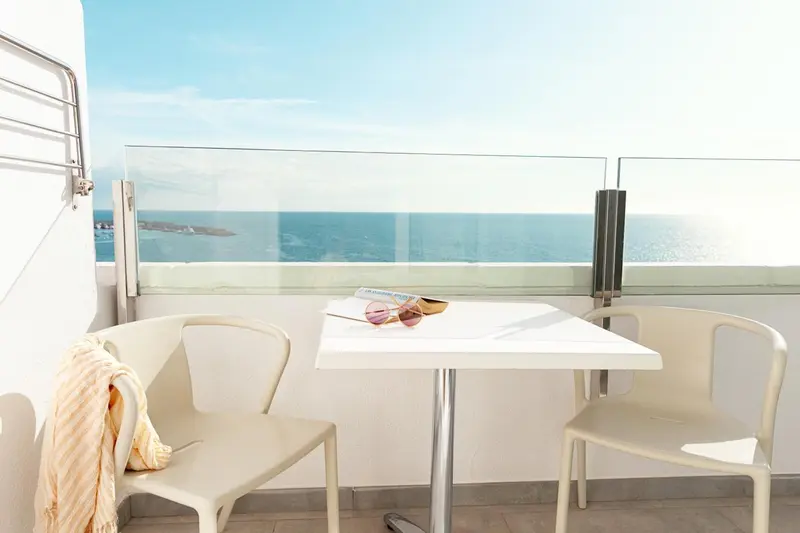 Une table et deux chaises blanches sur un balcon avec vue sur la mer.