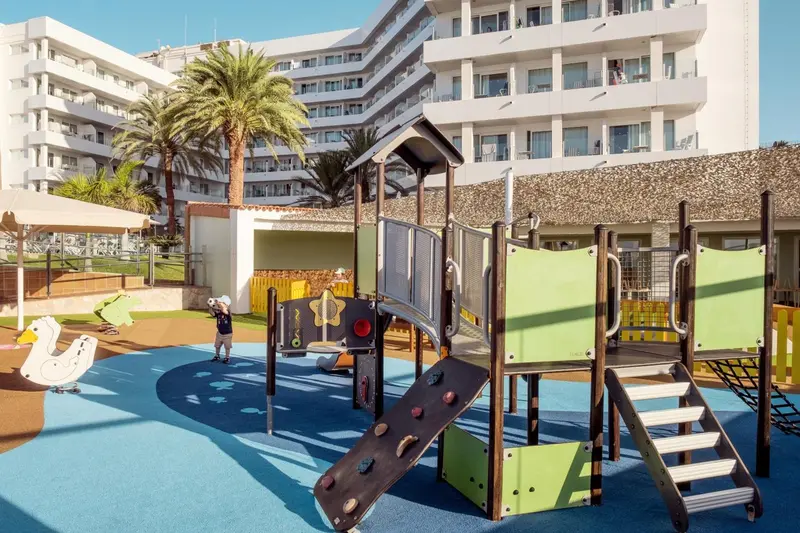 Aire de jeux colorée avec structures en bois et sol souple, devant un bâtiment blanc.