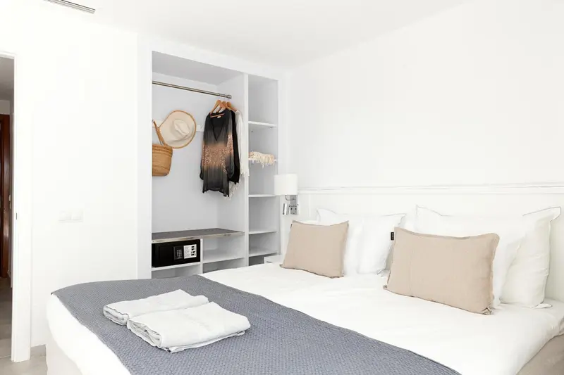 Une chambre lumineuse avec un lit fait et un placard ouvert.