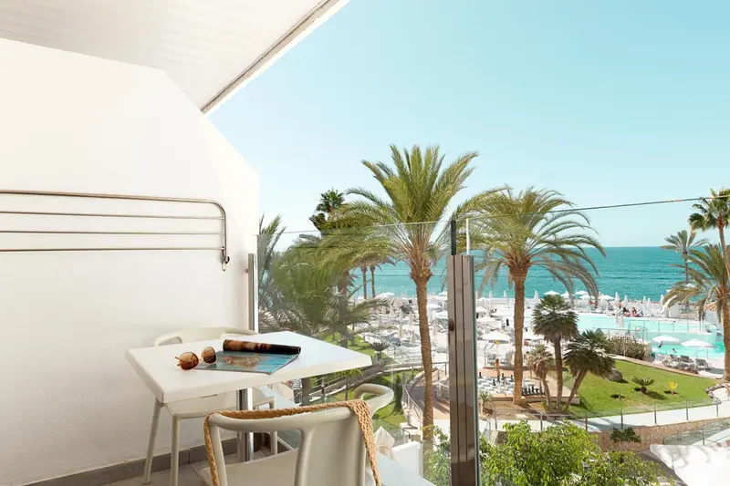 Une terrasse avec une table et des chaises offre une vue sur la mer et la végétation.