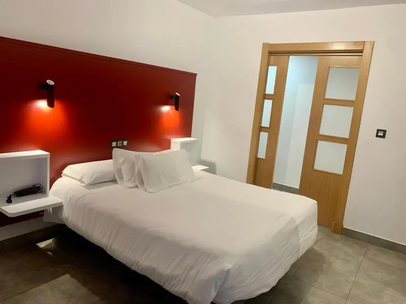 Une chambre lumineuse avec un lit blanc et un mur rouge.