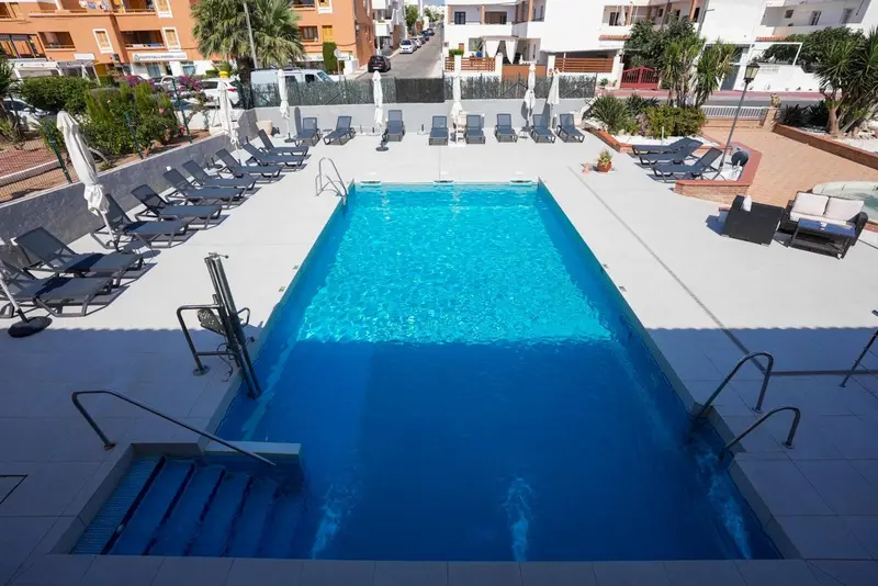 Une piscine rectangulaire entourée de chaises longues et de palmiers.